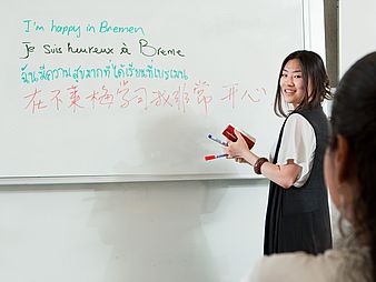 A person writes in different languages on a whiteboard.